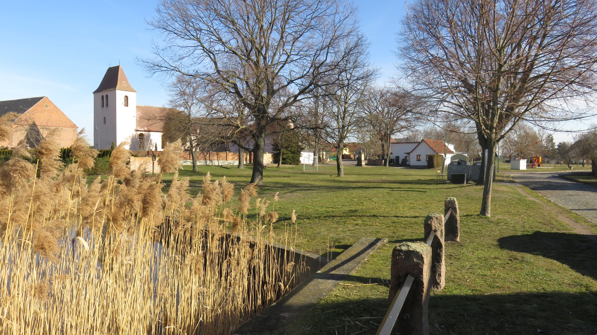 Das Foto zeigt den in der Ortsmitte gelegenen Anger mit Dorfteich sowie evangelischer Kirche und Ortsfeuerwehr im Hintergrund.