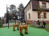 Wir schauen vom Schulhof aus auf unsere zwei Holzpferde zum Spielen und zwei Reckstangen in verschiedenen Höhen. Dahinter ist der Fußballplatz, und rechts das große Haus ist das Schulgebäude.